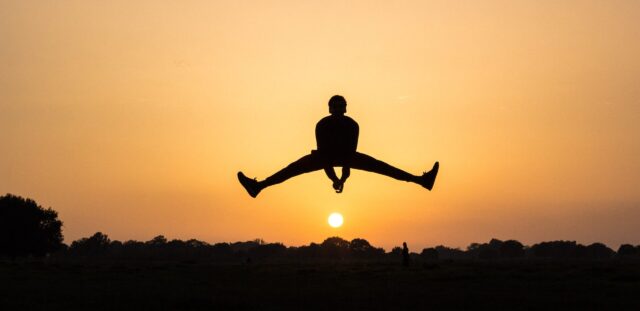 夕日を背景に喜びでジャンプしている男性